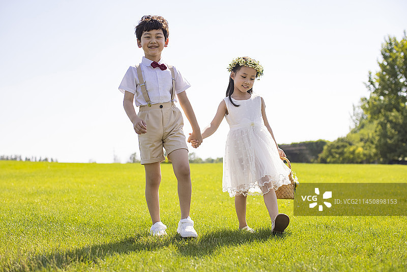 Cute flower girl and ring bearer playing on the grass图片素材