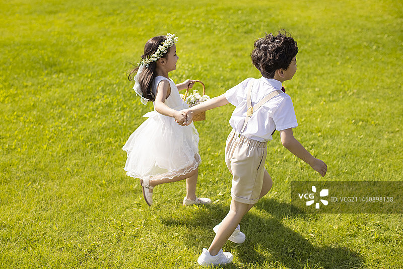 Cute flower girl and ring bearer playing on the grass图片素材