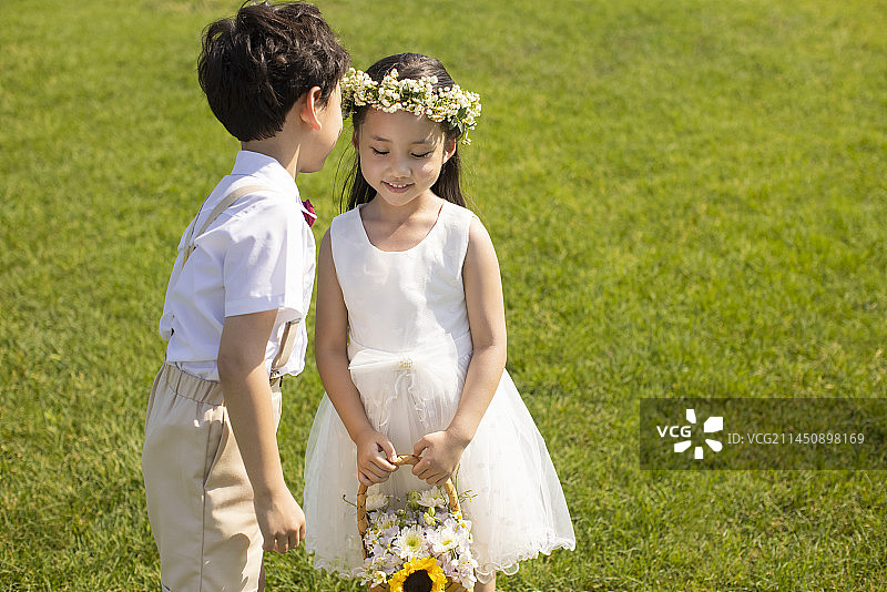 Cute flower girl and ring bearer playing on the grass图片素材