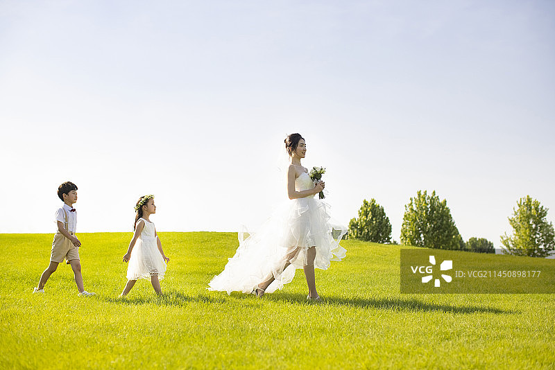 Beautiful Chinese bride walking through a park with flower girl and ring bearer following图片素材