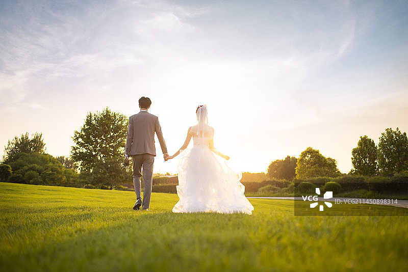 Happy bride and groom walking on the grass图片素材