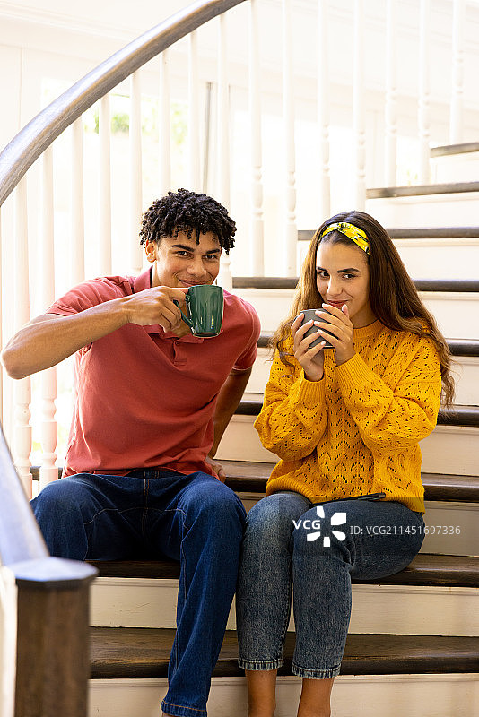 混血年轻夫妇在家中楼梯上喝咖啡，留白图片素材