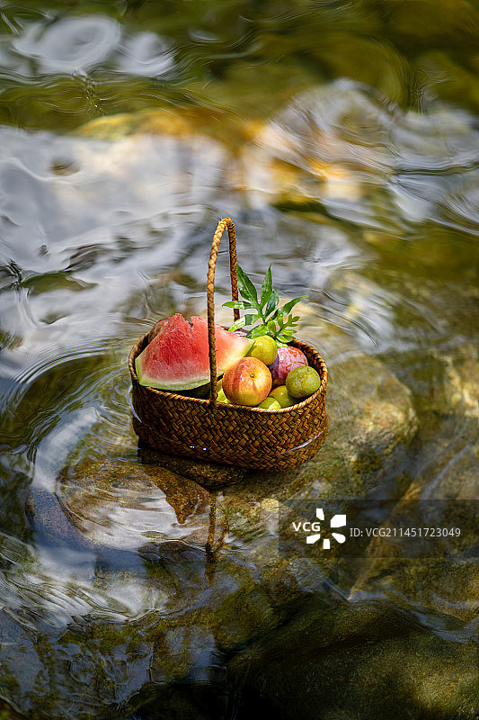 清澈的溪流中石头上摆放的果篮和西瓜图片素材