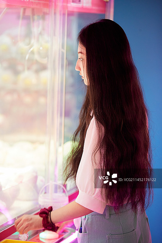 在电子游戏娱乐城玩抓娃娃机的时尚少女图片素材