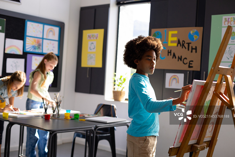 快乐的小学生在学校美术课上用画笔和画架绘画图片素材