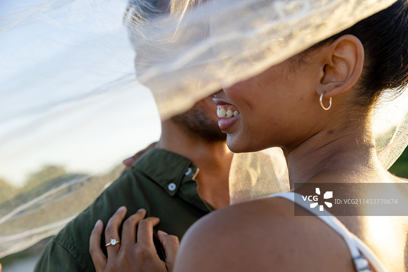 在海滩日落时分，戴着面纱的混血新婚夫妇浪漫特写图片素材