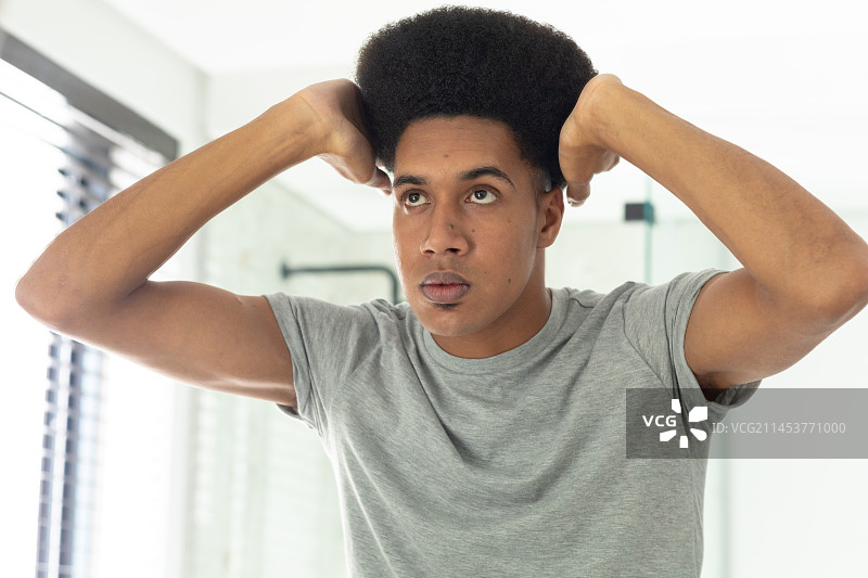 混血男人在阳光明媚的浴室里照镜子整理头发图片素材