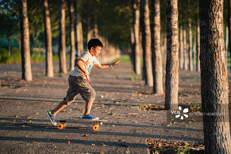 小男孩在夕阳下的街道玩滑板图片素材