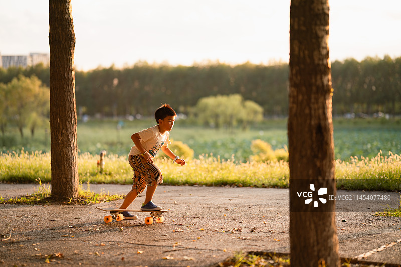 小男孩在夕阳下的街道玩滑板图片素材