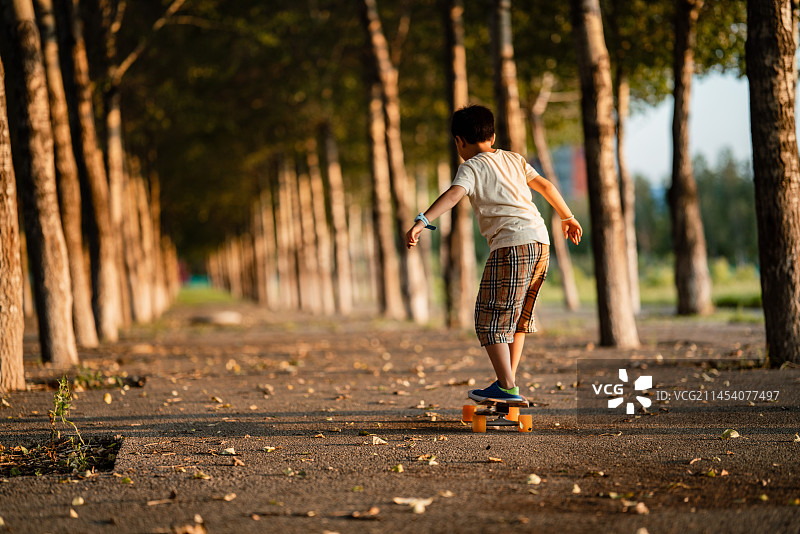 小男孩在夕阳下的街道玩滑板图片素材