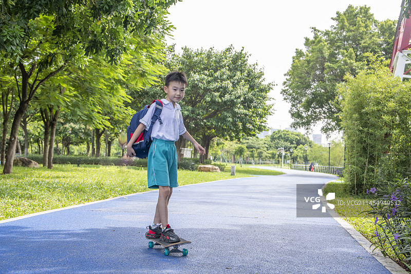 公园小路上背着书包玩滑板的小学生图片素材