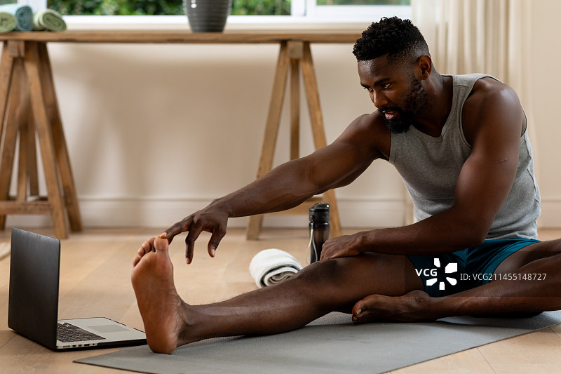 在家使用笔记本电脑练习瑜伽的非裔美国男人图片素材