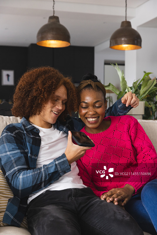 快乐情侣在客厅沙发上一起玩手机图片素材