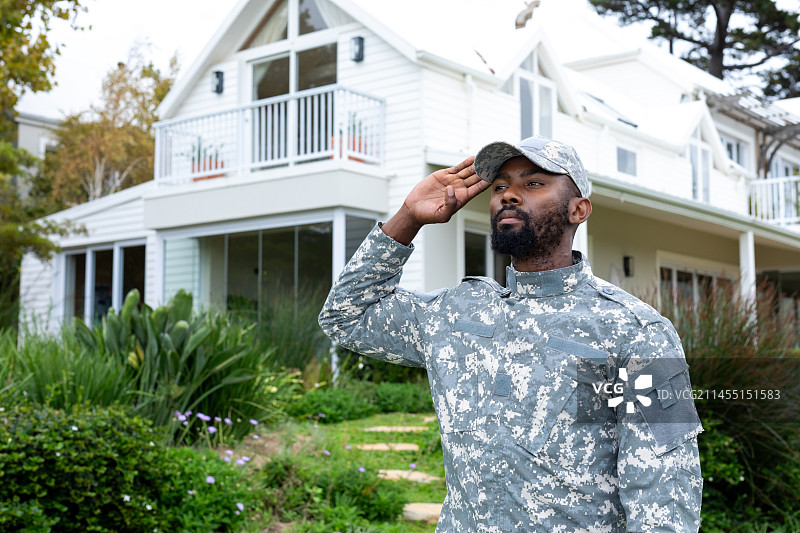 身穿军装的非裔美国男士兵敬礼并站在房子前图片素材
