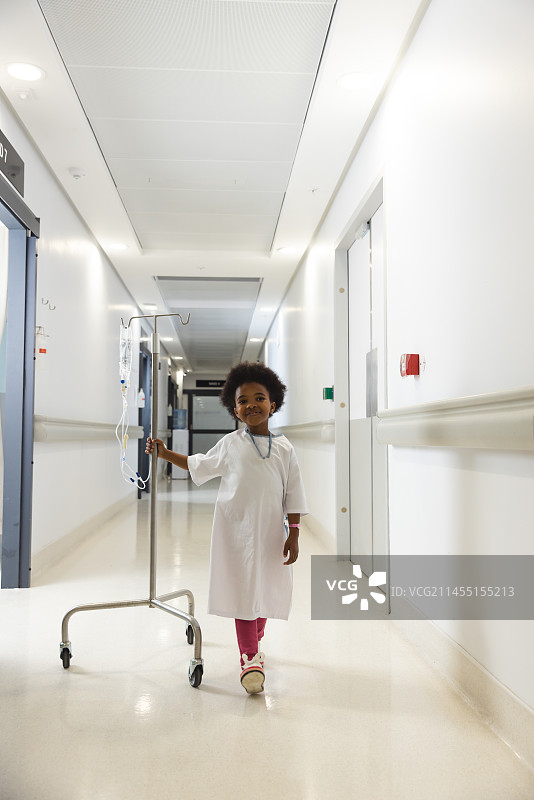 快乐的非洲裔美国女孩患者在医院走廊里拿着输液器行走图片素材