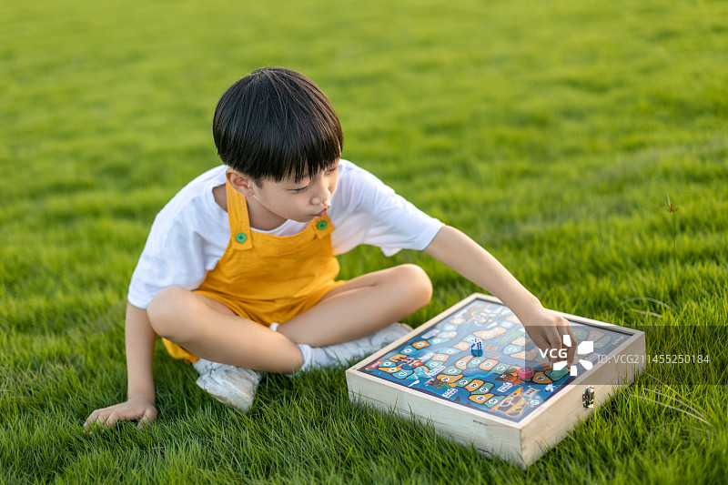 小男孩坐在秋天公园的草坪上下棋图片素材