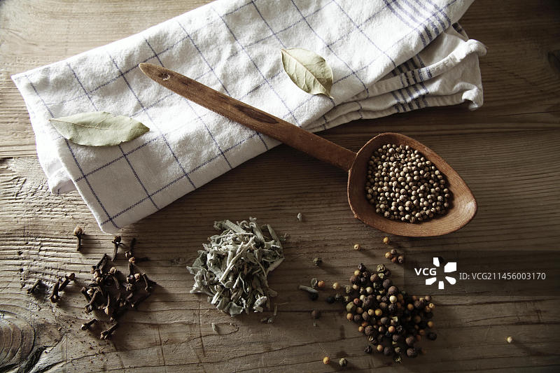 香菜、胡椒粒、鼠尾草和干丁香与木勺和厨房用巾在乡村木质表面上图片素材