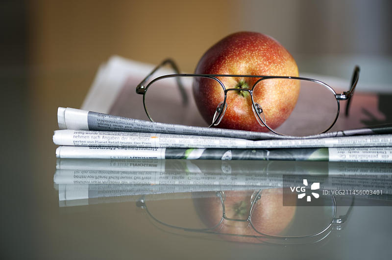 放在玻璃桌上的苹果、报纸和眼镜图片素材