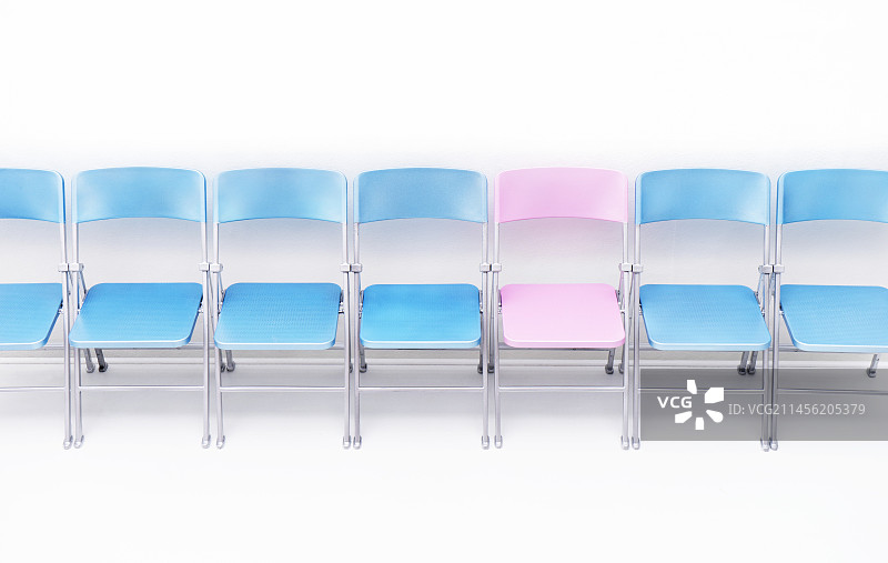 一排蓝色椅子中的一把粉色椅子图片素材