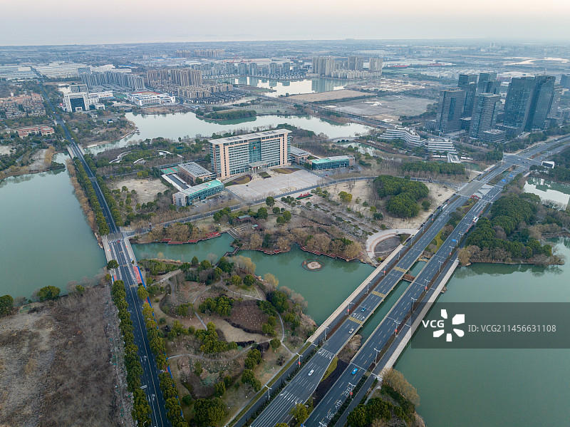 航拍西山漾湿地的日出时分，天空露出鱼肚白和温暖的朝霞，平静的水面倒影着吴兴区体育馆和华美达酒店等建筑图片素材