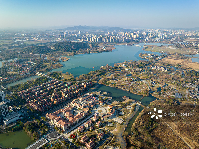 航拍西山漾湿地的日出时分，温暖的朝阳照射到湿地公园的建筑和绿化，平静的湖面倒影着蓝天图片素材