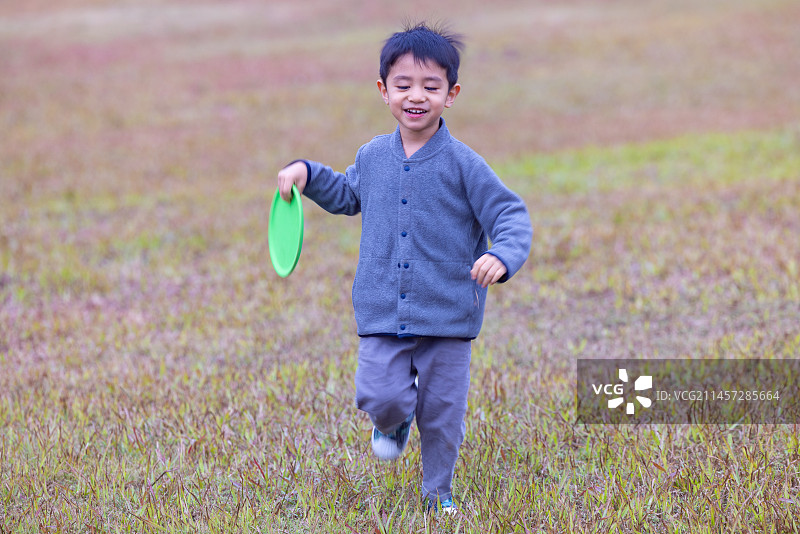 一个小男孩在公园的草地上玩飞盘图片素材