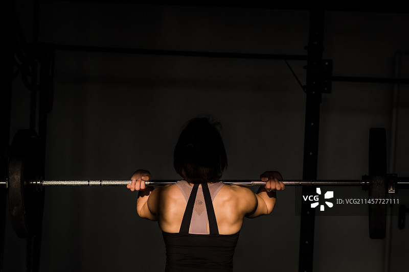 在德国昏暗的健身房里，年轻女子举起杠铃的背影图片素材