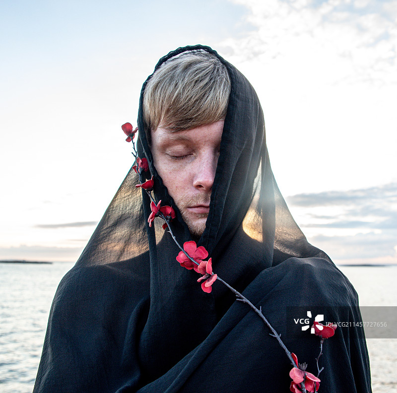 手持红色花枝，站在湖边的年轻男子特写，挪威弗雷德里克stad，人与自然的共生图片素材
