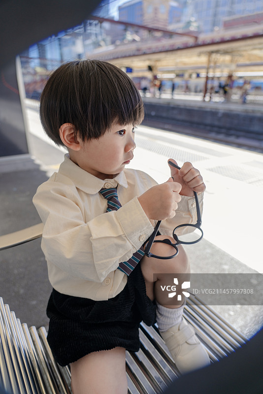 火车站座椅旁摆弄眼镜的戴领带小男孩图片素材
