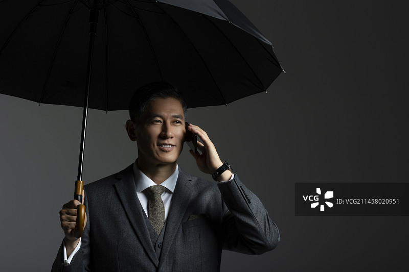 中年商务男士撑着雨伞打电话图片素材