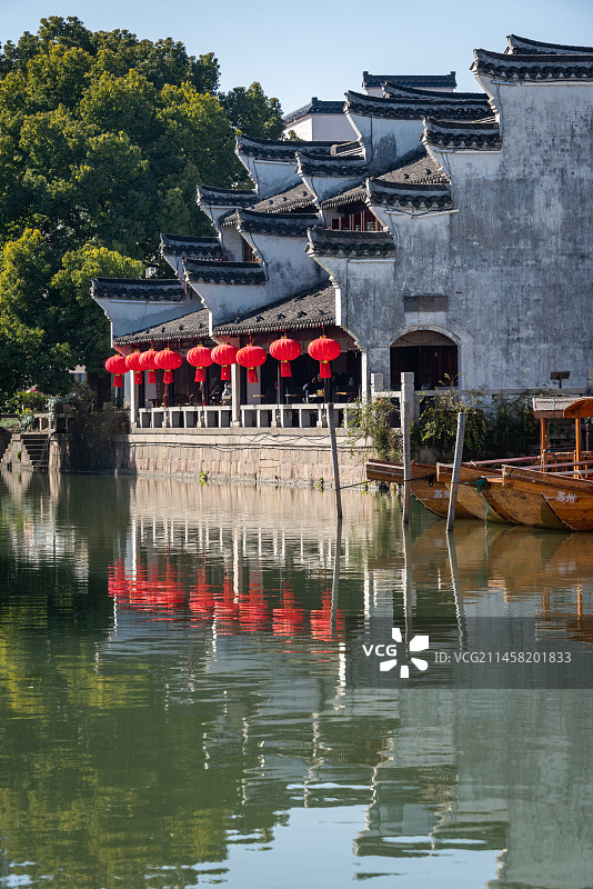初春的安静的江南古镇震泽古镇一景，绿树掩映下白墙灰瓦的传统民居和大红灯笼，倒影到平静的小河里图片素材