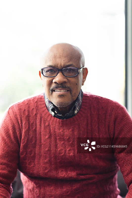 戴着眼镜坐在家里的沙发上的年长混血男性肖像图片素材