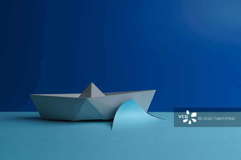 蓝色背景中破纸前行的轮船微缩创意特写照图片素材