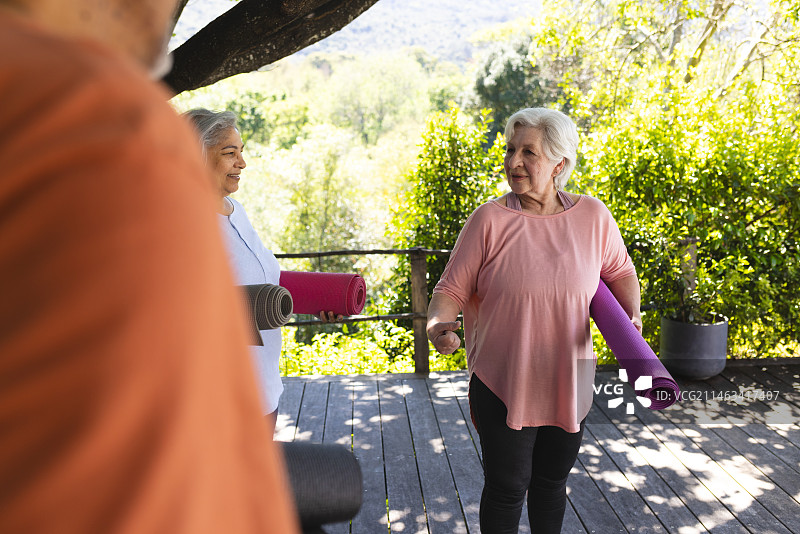 快乐的白人老年妇女拿着运动垫，在阳光明媚的花园里与朋友们交谈图片素材
