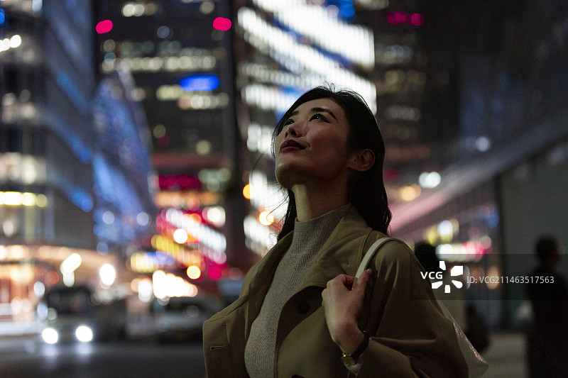夜晚高知商务女子在城市街道上仰头欣赏城市夜景图片素材