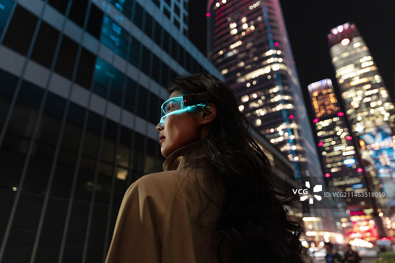 夜晚未来女子戴着智能眼镜在城市街道上，感知未知世界图片素材