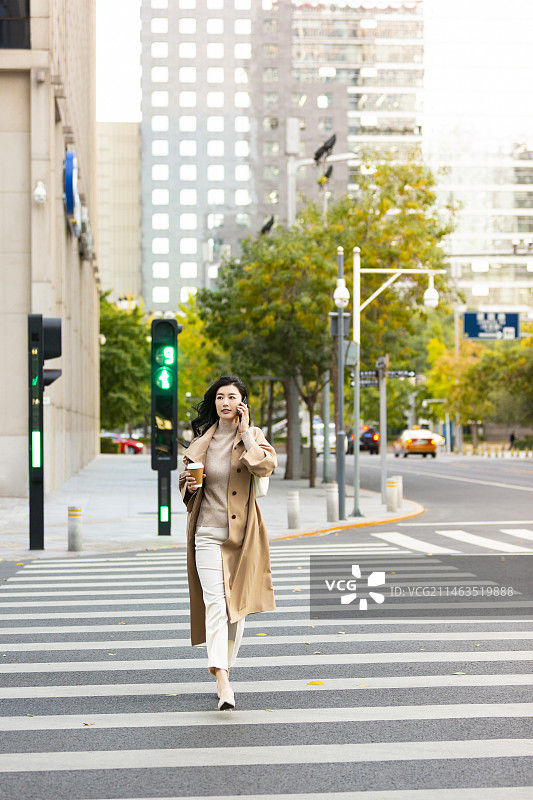 高知女商人拿着咖啡、打电话过马路图片素材
