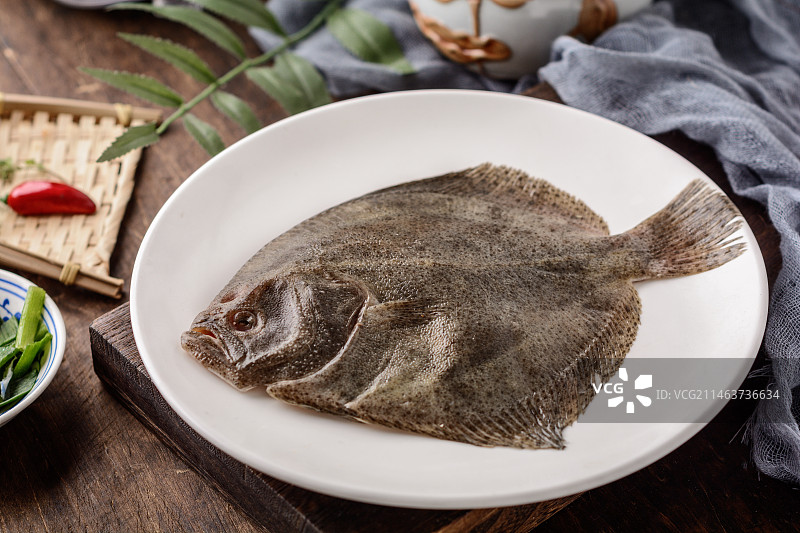 木纹桌上白色瓷盘里的一条新鲜多宝鱼图片素材