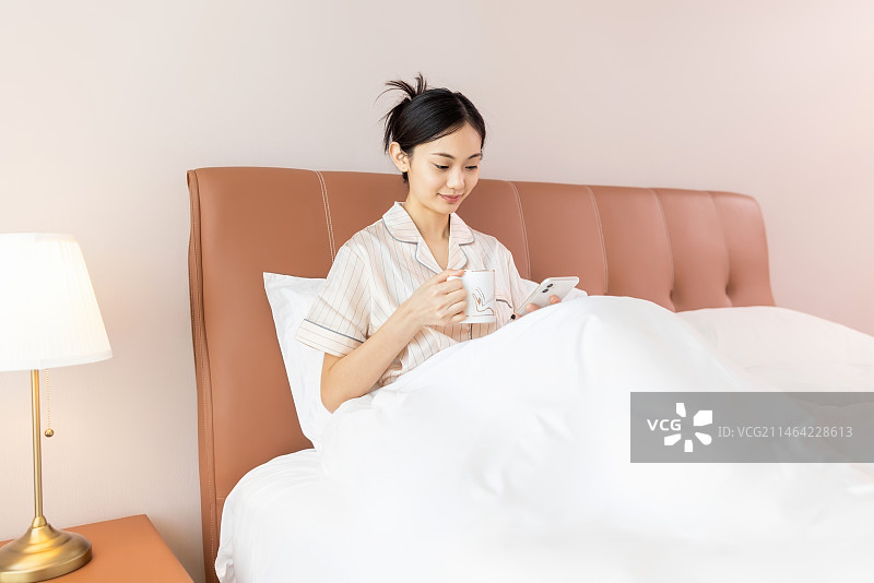 年轻的女孩在床上玩手机图片素材