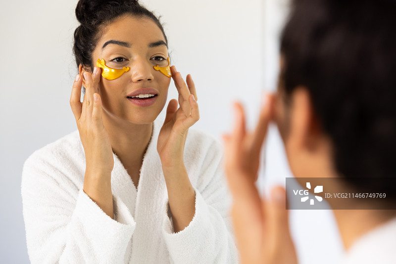 阳光明媚的浴室里，混血女人穿着浴袍敷眼膜图片素材