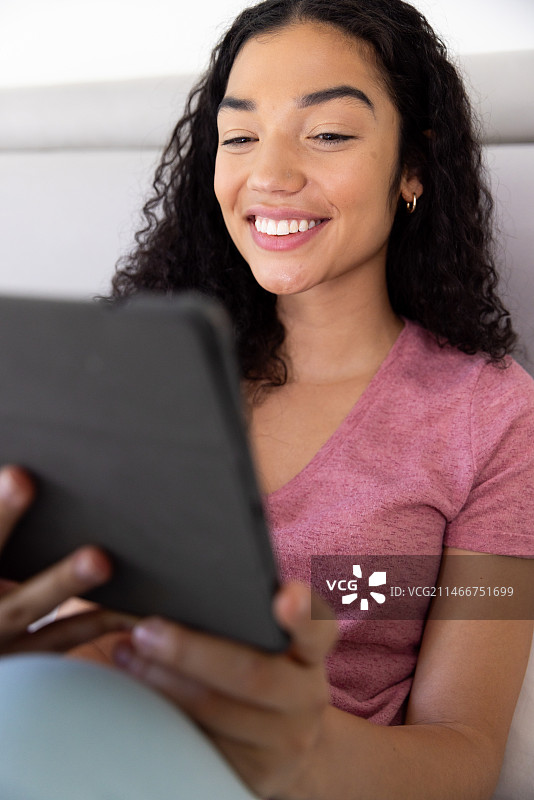 快乐的混血女人在阳光明媚的家里使用平板电脑坐在床上图片素材