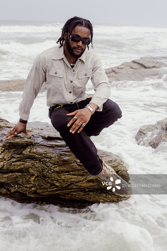 年轻男人坐在加纳阿克拉海滩的岩石上图片素材