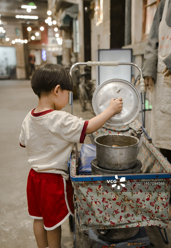 小男孩打开小拉车里的旧锅子盖子图片素材