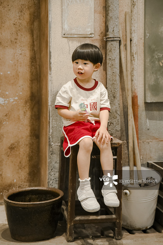 小男孩坐在老房子门口的高脚方木凳上图片素材