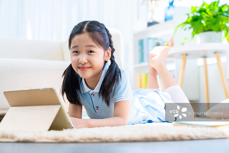 小女孩趴在地毯上使用平板电脑图片素材