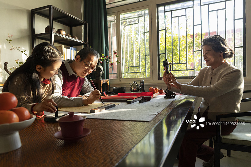 东方家庭过年：爷爷教孙女在书房写毛笔字，奶奶给他们拍照图片素材