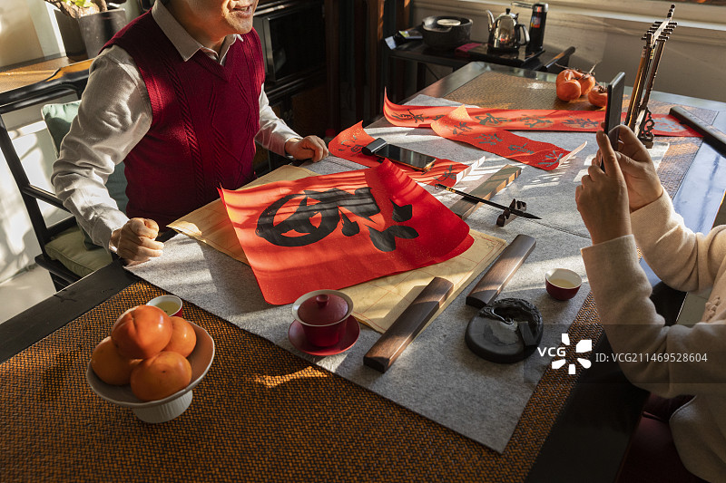 东方家庭过年：老年丈夫在书房写毛笔字，老年妻子给他拍照、录视频特写图片素材