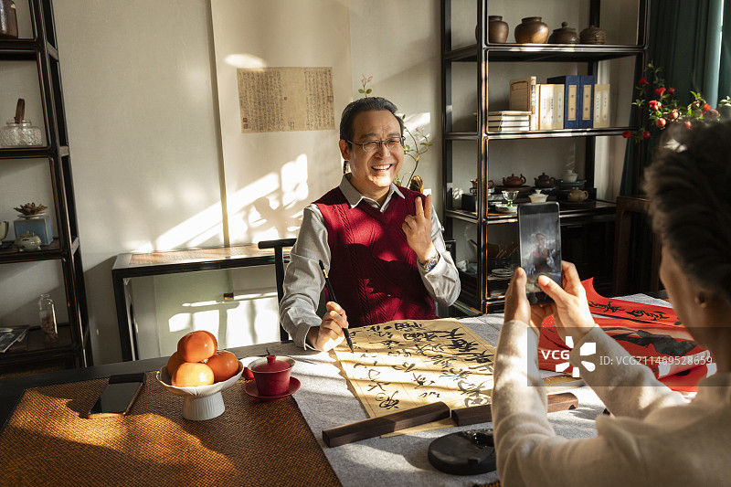 东方家庭过年：老年丈夫在书房写毛笔字，老年妻子给他拍照图片素材