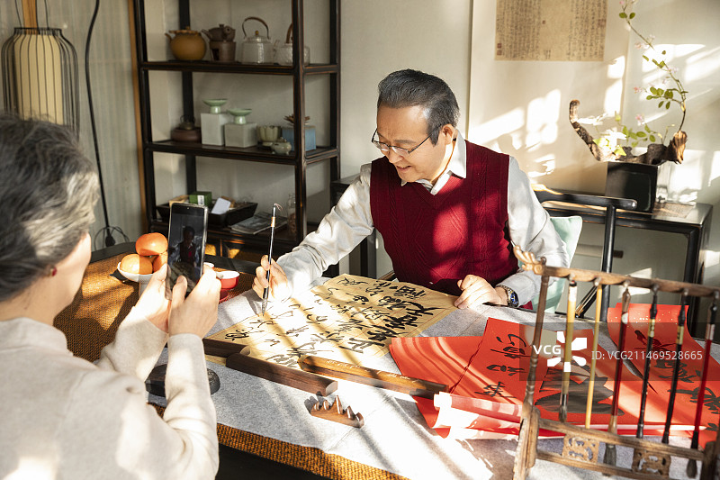 东方家庭过年：老年丈夫在书房写毛笔字，老年妻子给他拍照、录视频图片素材