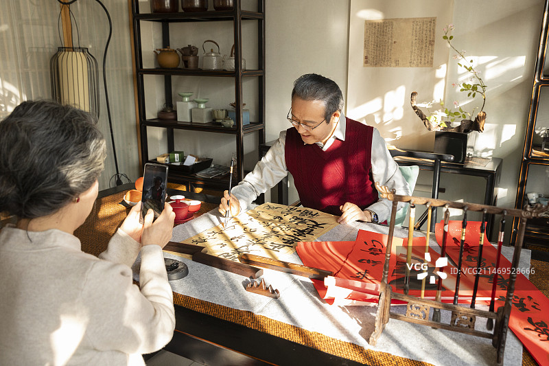 东方家庭过年：老年丈夫在书房写毛笔字，老年妻子给他拍照、录视频图片素材
